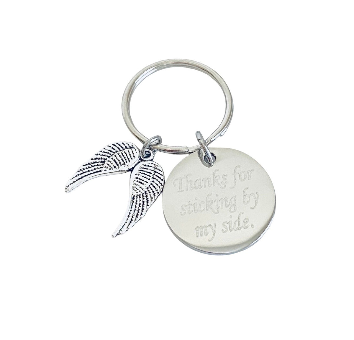 A silver-toned metal keychain featuring a round engraved disc that reads 'Thanks for sticking by my side.' and a textured wing charm, shown on a plain white background.