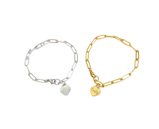 Two paperclip chain bracelets on a white background, one silver-tone with a small heart charm and one gold-tone with a small heart charm.