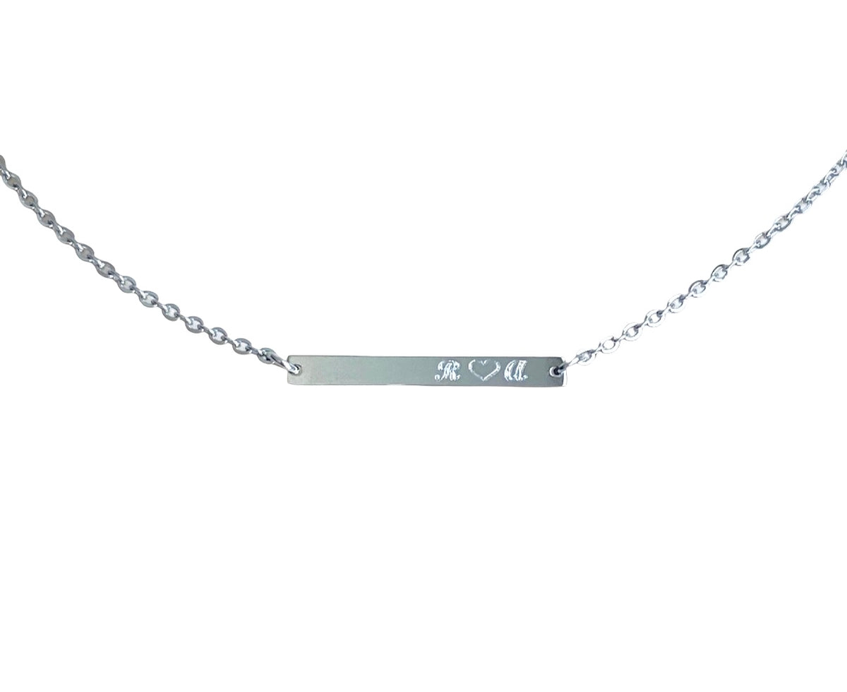 A silver bar necklace with a delicate cable chain, featuring custom engraved initials 'K & M' on the polished center bar, shown against a plain white background.