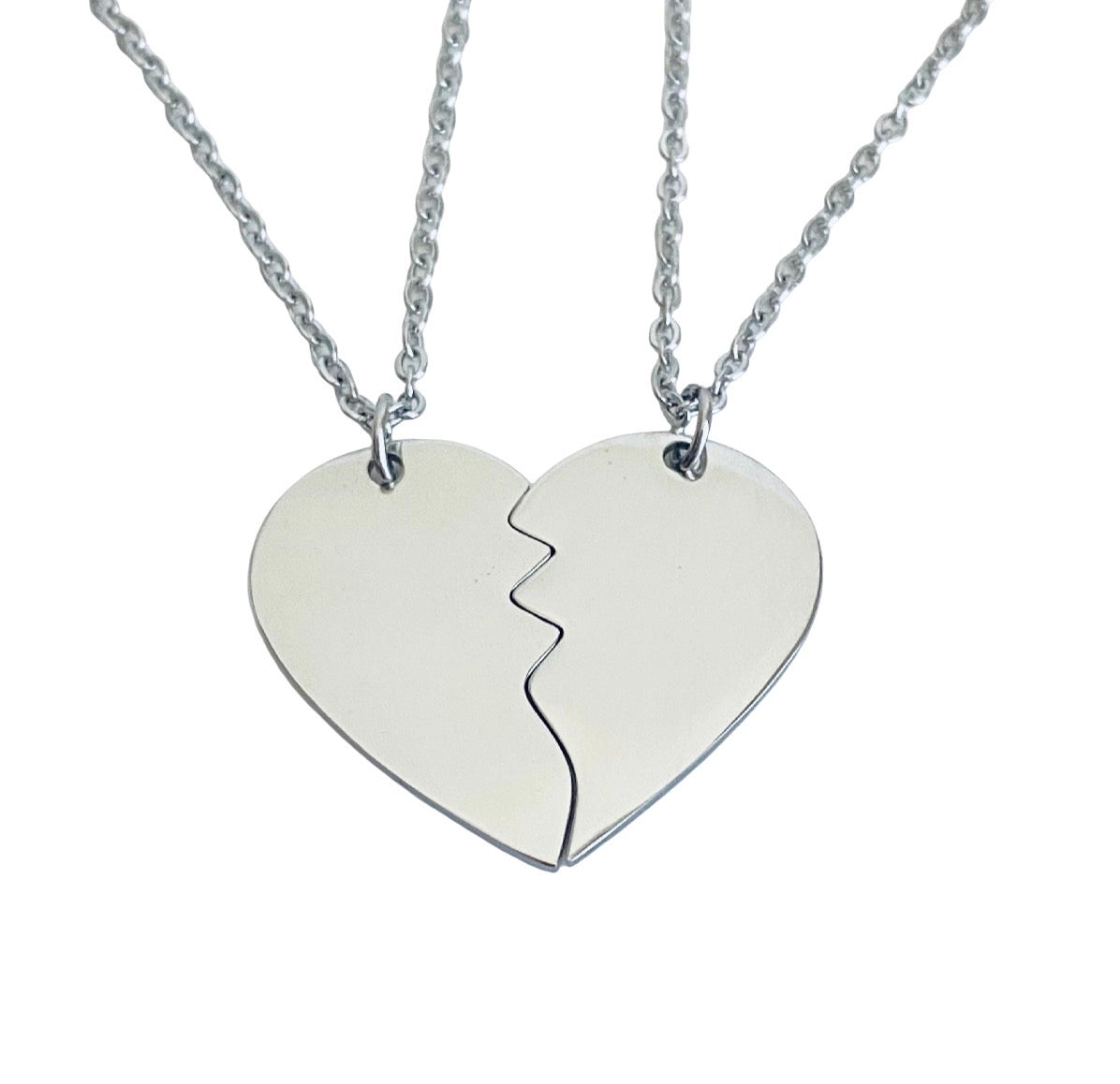 Two silver chain necklaces with matching half-heart pendants that fit together like a broken heart, shown on a plain white background.