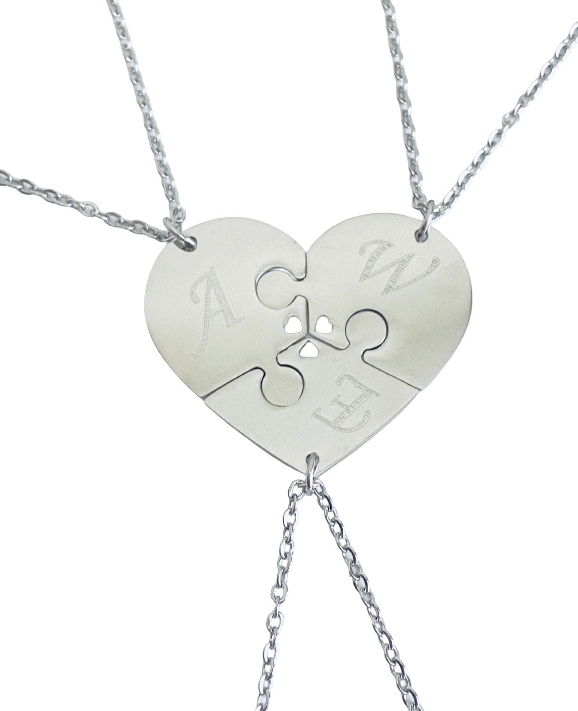 Three silver puzzle heart necklaces that fit together to form one heart, each engraved with a letter, on a white background.