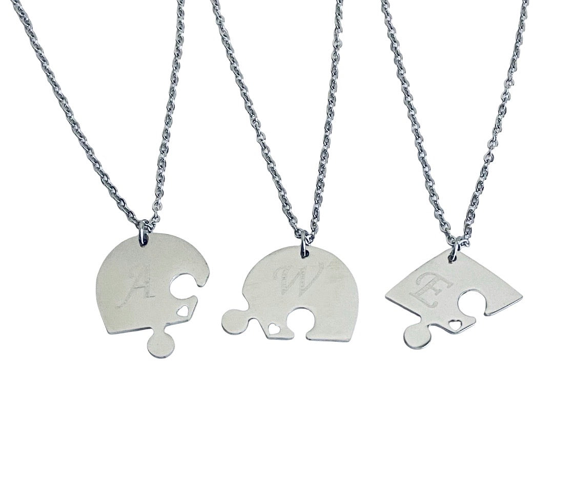 Three silver puzzle-piece necklaces with chain links, each engraved with a different letter (A, W, and E), displayed on a clean white background.
