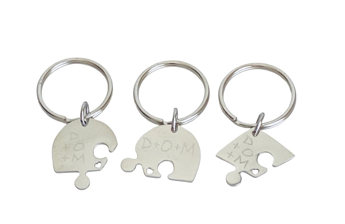 Three silver metal keychains with puzzle-shaped charms engraved with 'D+O+M', displayed on a plain white background.