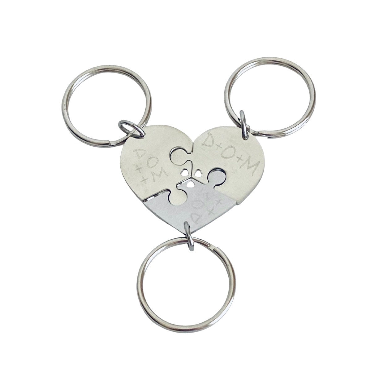 Three-piece silver metal keychain set forming a heart-shaped puzzle with individual key rings, engraved with 'D+O+M' and 'A+Q+M' on a white background.