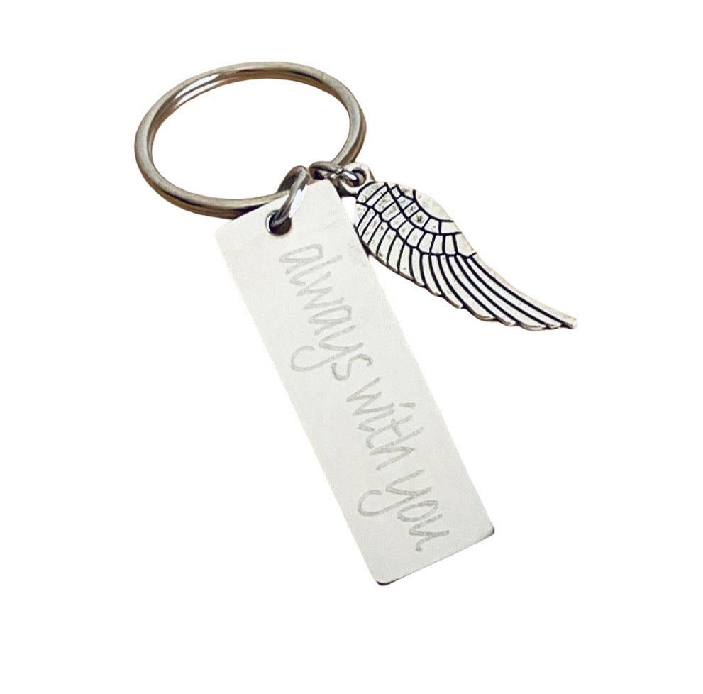 A silver-toned metal keychain featuring a rectangular engraved tag with the words 'always with you' in cursive and a small wing charm, shown on a plain white background.