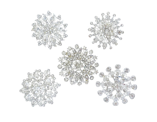 Five silver snowflake-shaped brooches embellished with clear crystals, arranged on a plain white background.