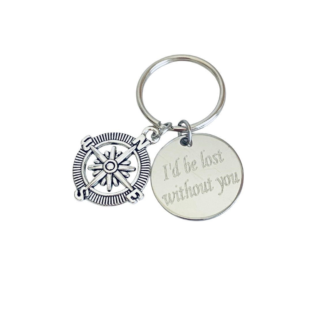 A silver-toned metal keychain featuring a compass-shaped charm and a round disc charm engraved with the phrase 'I'd be lost without you', shown on a plain white background.
