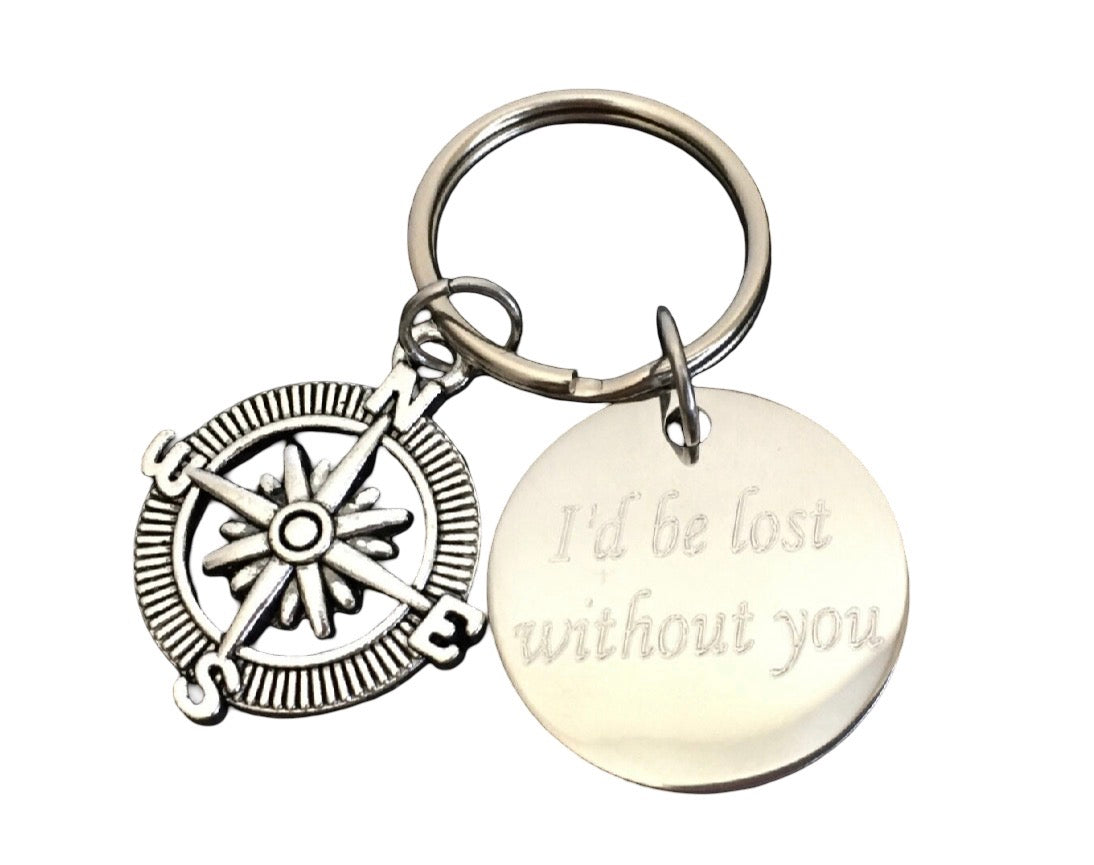 A silver-toned metal keychain featuring a compass rose charm and a round disc charm engraved with the words 'I'd be lost without you', shown on a plain white background.