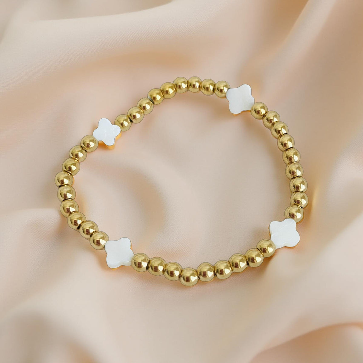 Gold beaded bracelet with white star-shaped beads on a soft beige background