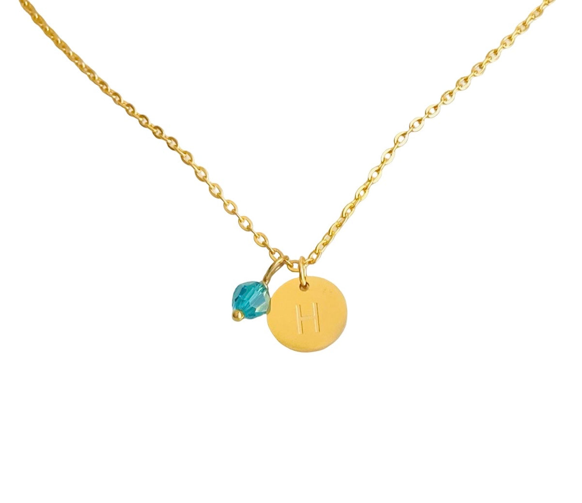 A gold chain necklace featuring a round gold disc pendant engraved with the letter 'H' and a small faceted blue crystal charm, shown on a plain white background.