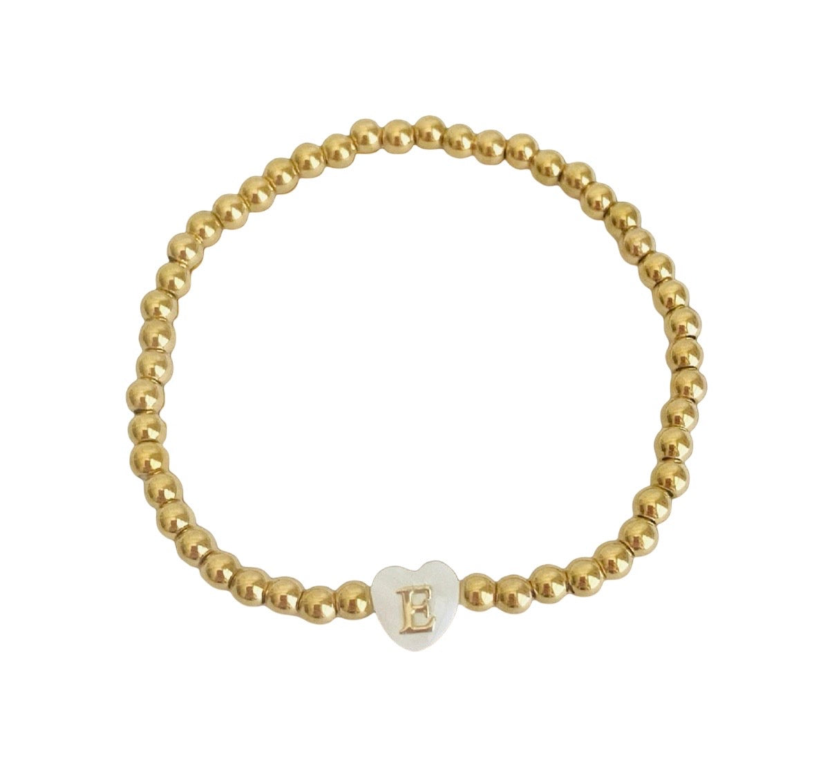 A gold beaded stretch bracelet featuring a small white heart-shaped charm with a gold letter 'E' on it, displayed on a clean white background.