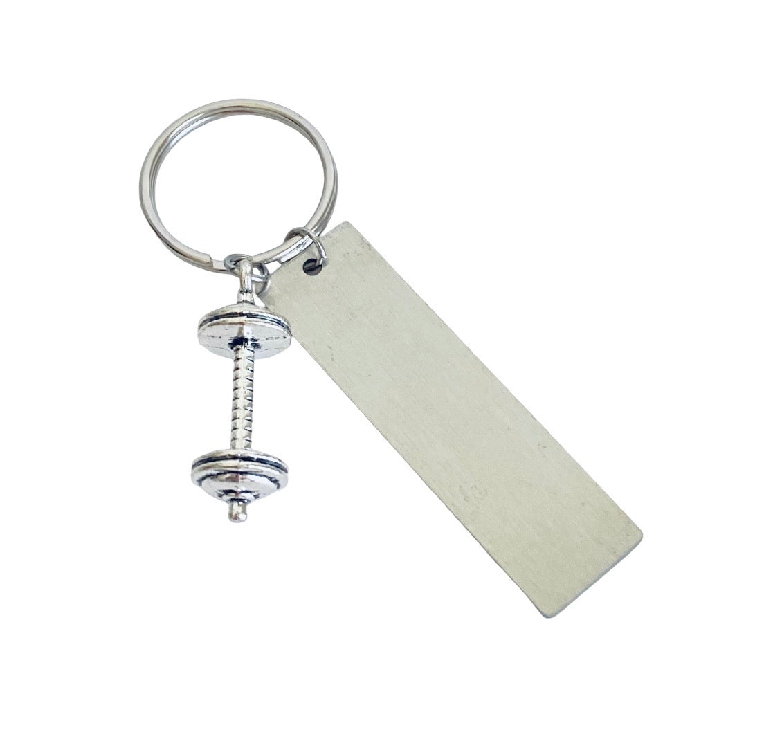 A silver metal keychain featuring a dumbbell-shaped charm and a blank rectangular tag, shown on a plain white background.