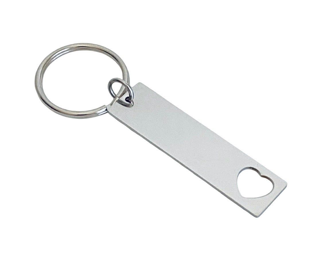 A silver metal keychain featuring a rectangular tag with a heart-shaped cutout and a small heart-shaped hole near the top, attached to a split key ring.
