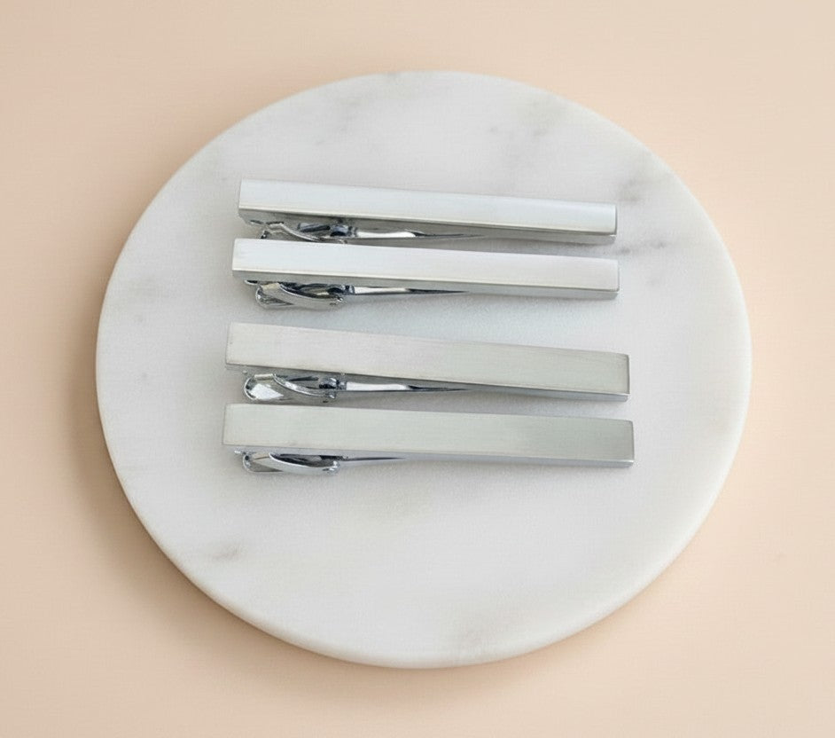Four silver metal hair barrette clips arranged on a round white marble tray against a soft peach background.