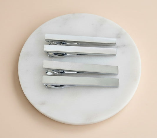 Four silver metal hair barrette clips arranged on a round white marble tray against a soft peach background.
