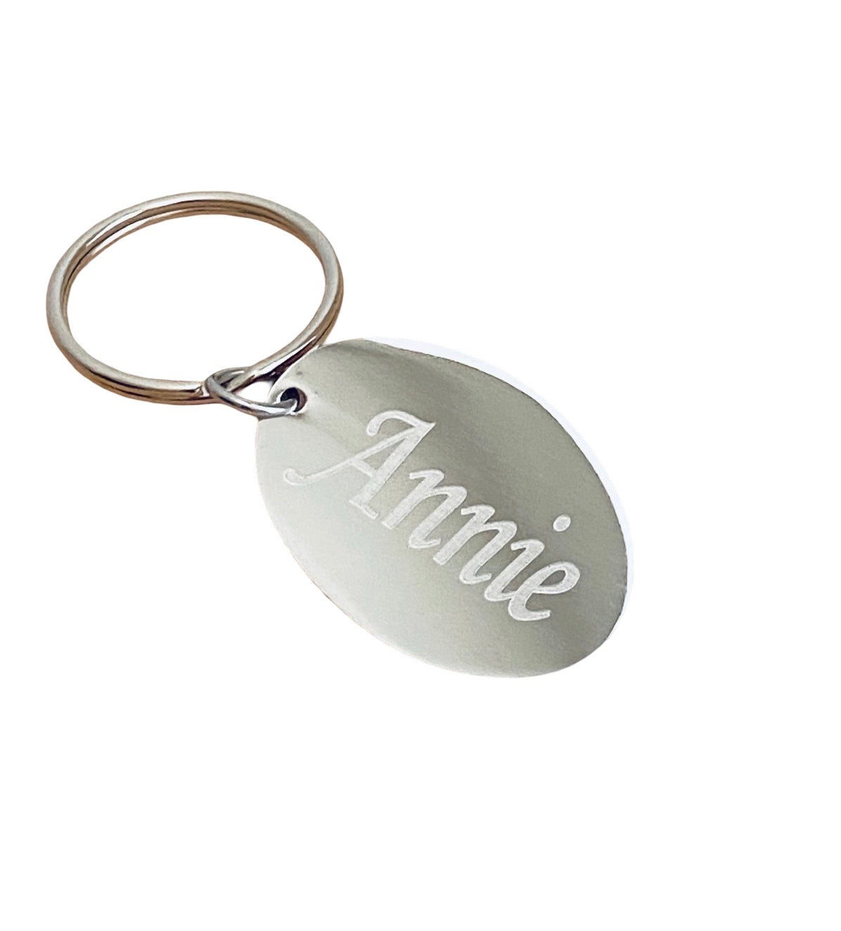 A silver oval metal keychain engraved with the name 'Annie' in cursive script, attached to a split key ring on a plain white background.