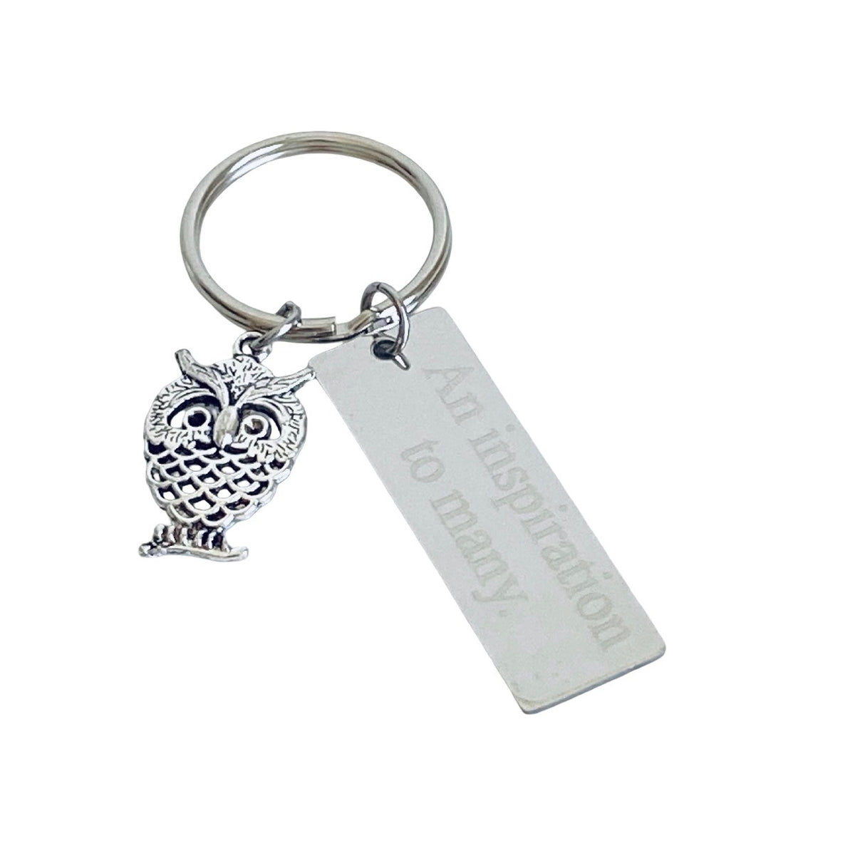 A silver metal keychain featuring an owl charm and a rectangular engraved tag that reads 'An inspiration to many,' shown on a plain white background.