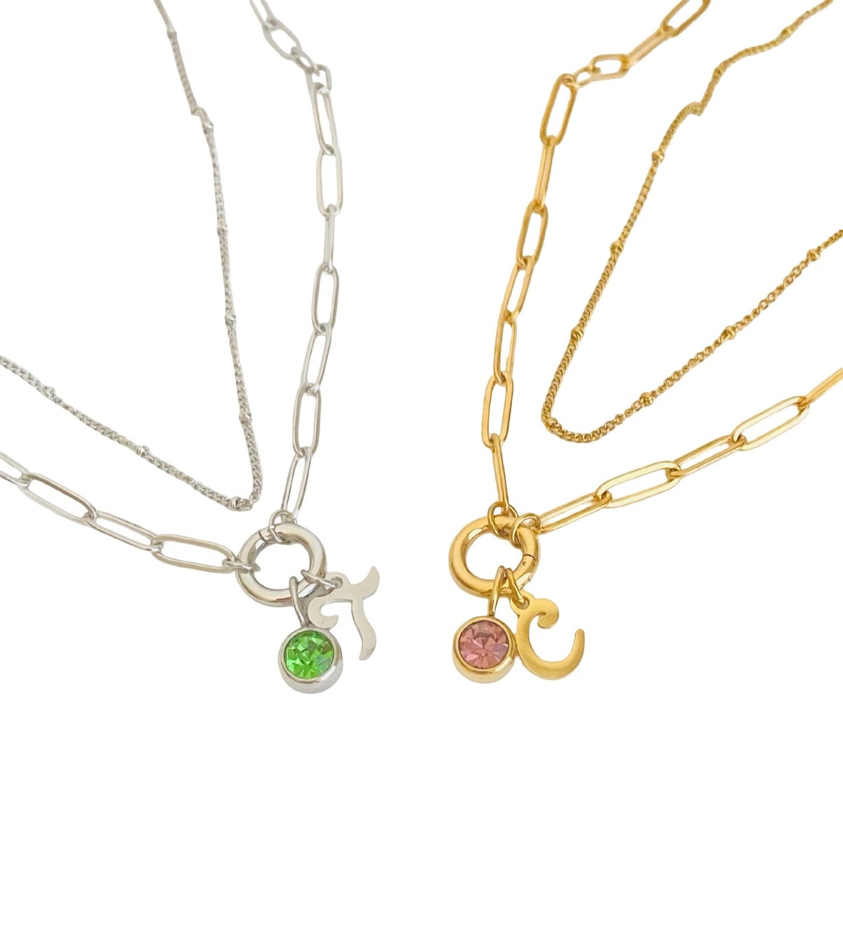 Two paperclip chain necklaces with zodiac sign pendants, one in silver with a green gemstone and one in gold with a pink gemstone, displayed on a white background.