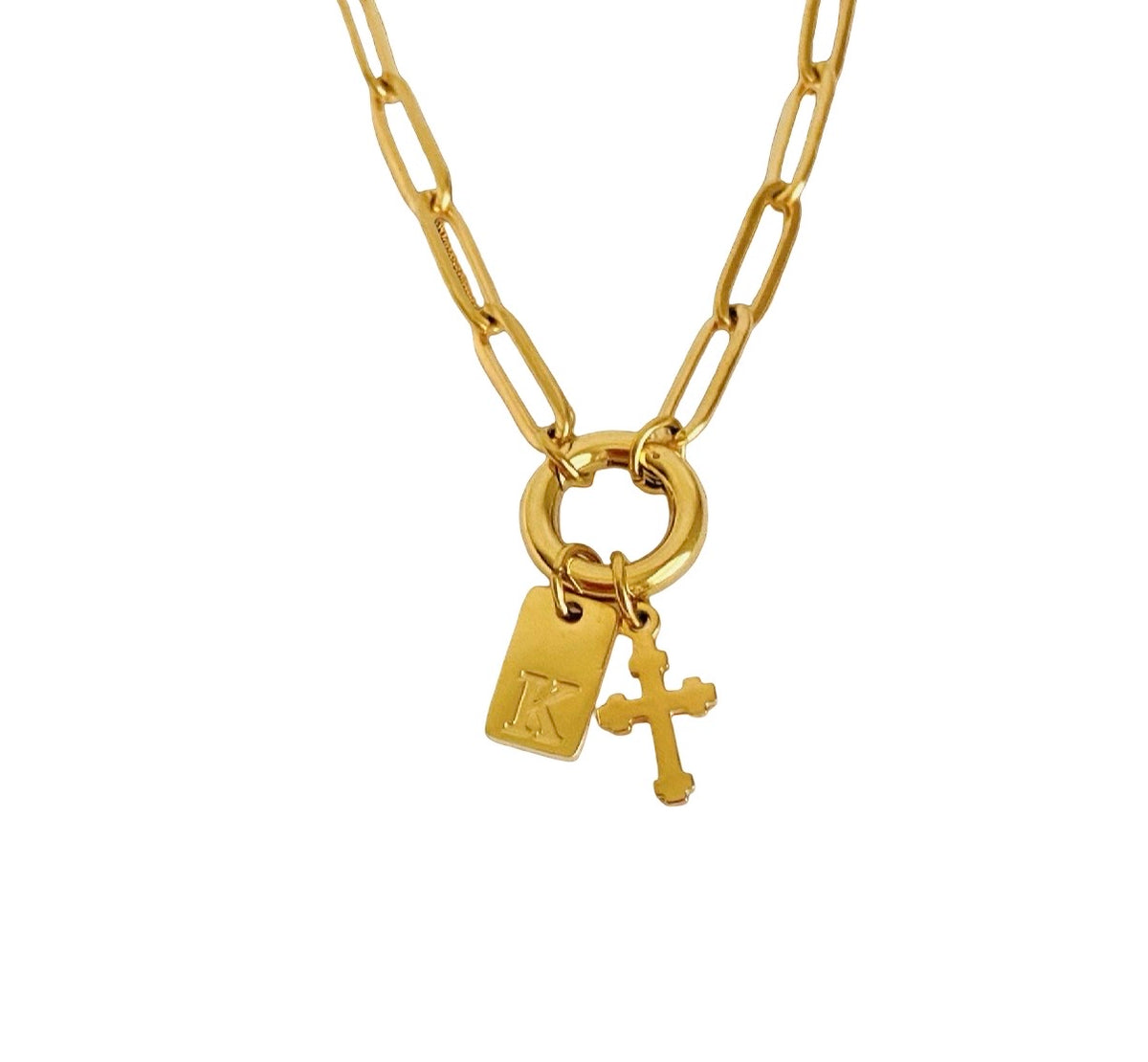 A gold paperclip chain necklace featuring a ring with a rectangular tag charm marked with a letter 'K' and a small cross charm, shown on a plain white background.