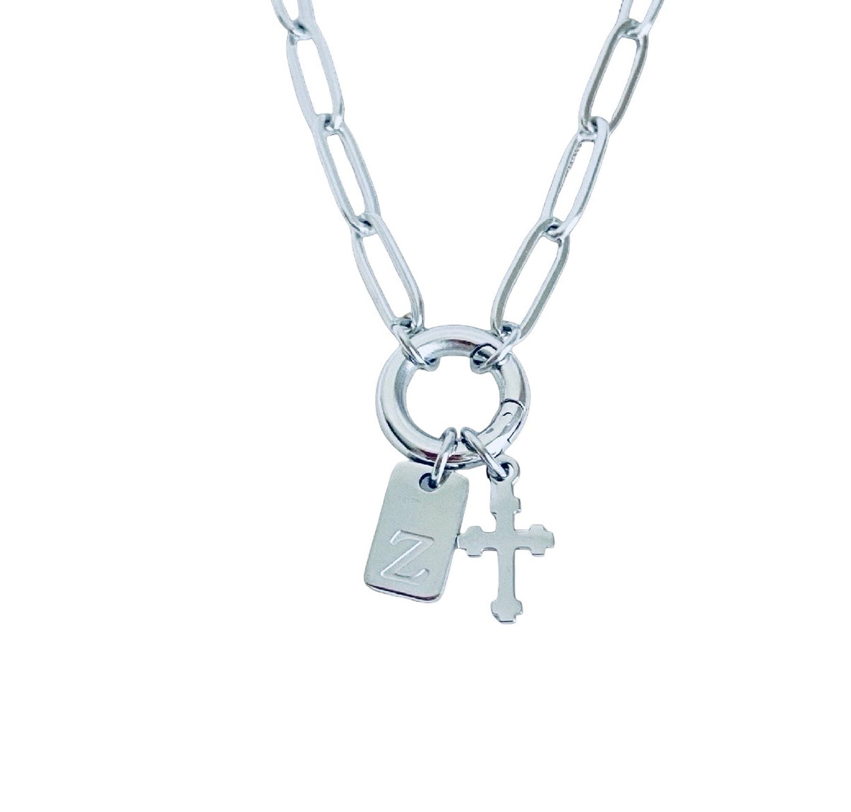A silver paperclip chain necklace with a ring clasp, featuring a rectangular engraved tag with a letter 'Z' and a small cross charm, shown on a plain white background.