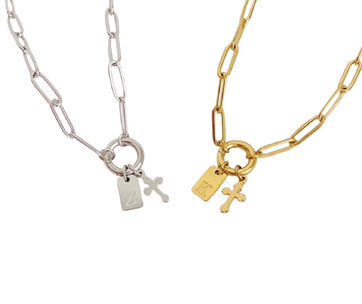 Two paperclip chain necklaces with small rectangular tags and cross pendants, shown side by side on a white background. One necklace is silver-toned and the other is gold-toned.