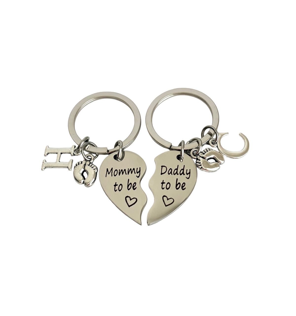 Two silver keychains shaped like half-hearts with 'Mommy to be' and 'Daddy to be' text on a white background.