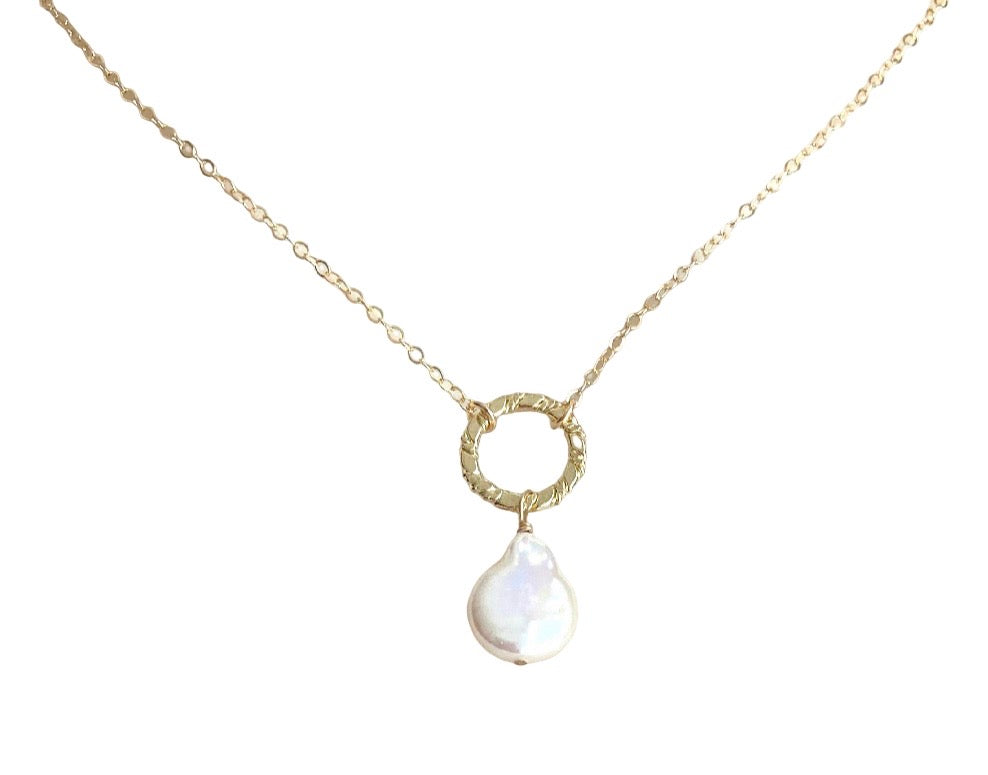 A delicate gold chain necklace featuring a textured circular ring pendant with a teardrop-shaped white iridescent shell drop, shown against a plain white background.