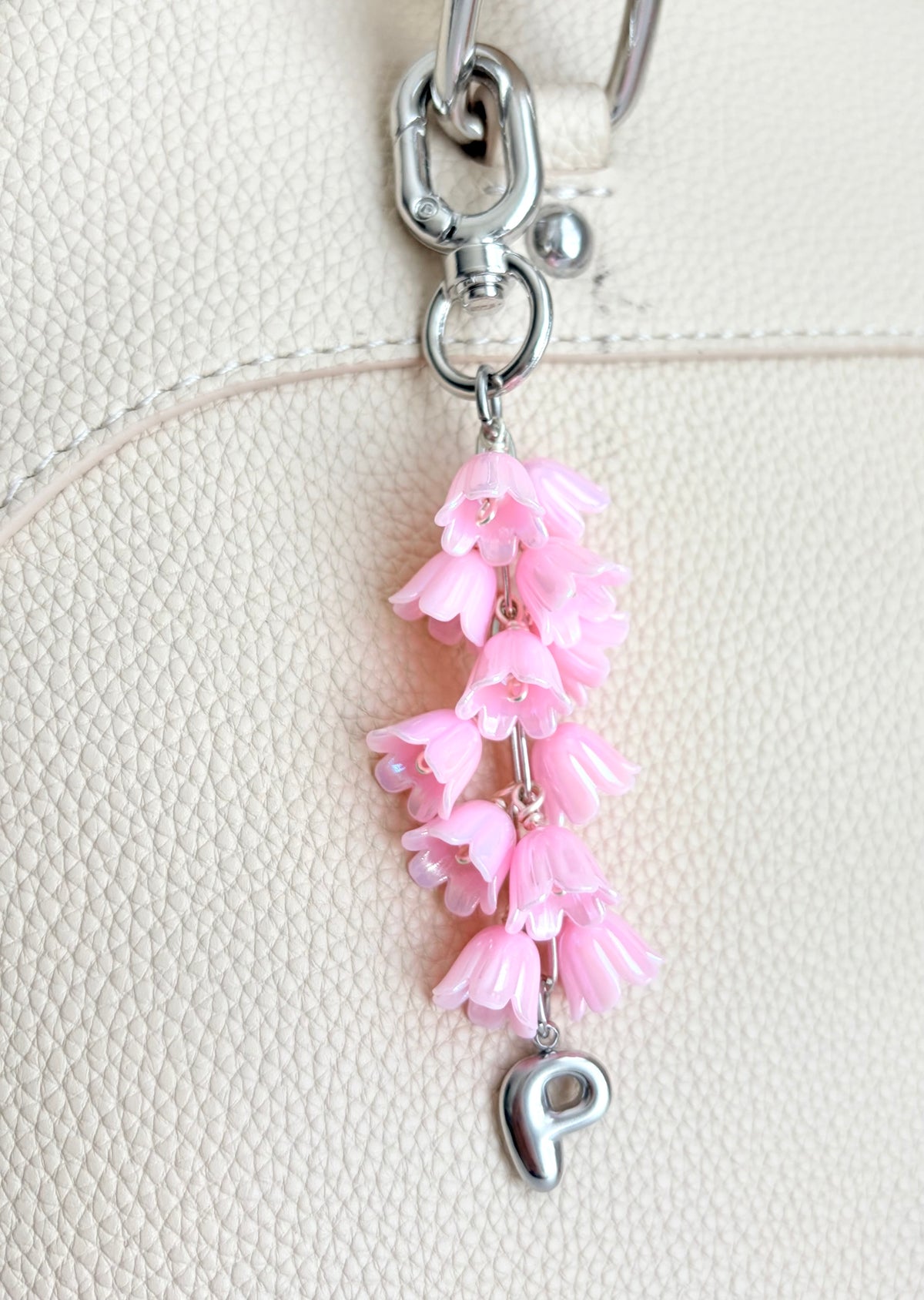 Pink floral keychain with a silver 'P' charm on a beige background