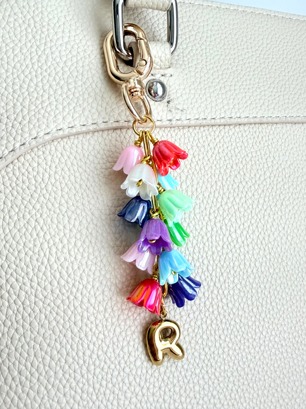 Colorful floral keychain with letter 'R' attached to a beige handbag.