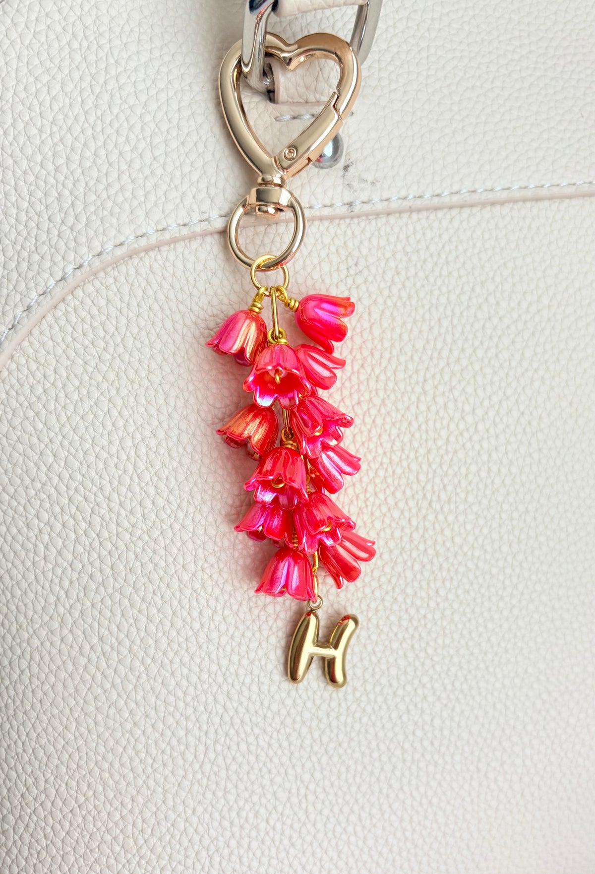 Pink floral keychain with a gold 'H' on a white background