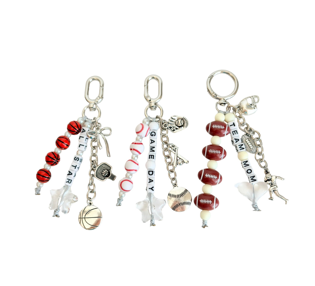 Three customized sports-themed keychains with silver-tone chains and charms, featuring red and white basketballs, footballs, baseballs, stars, and text reading 'ALL STAR', 'GAME DAY', and 'TEAM MOM' on a plain white background.
