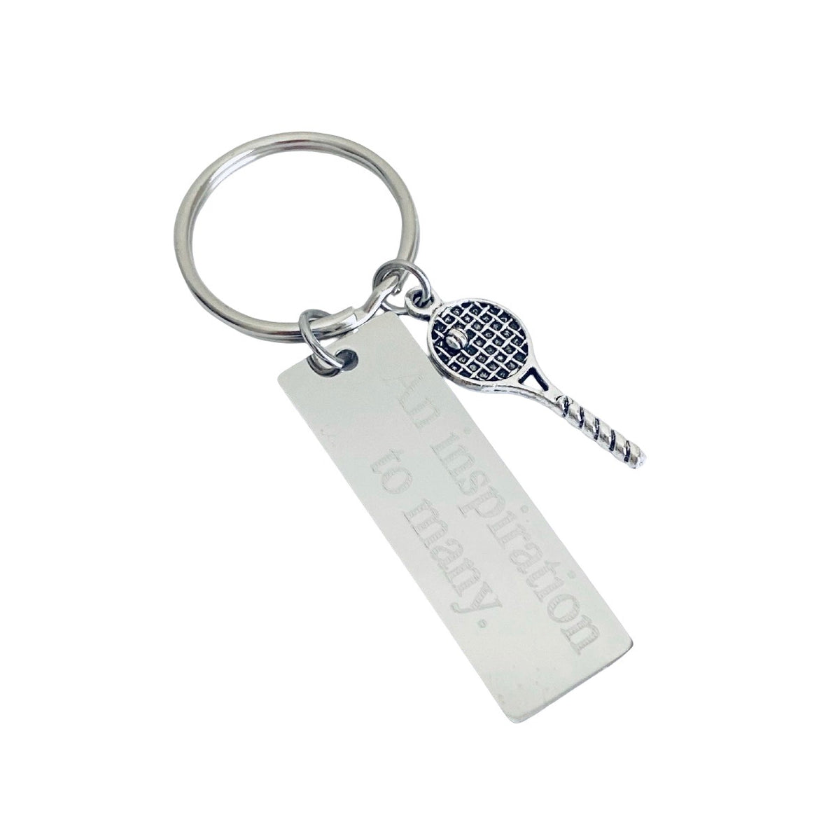 A silver metal keychain featuring a rectangular engraved tag with the words 'Your inspiration to many.' and a small tennis racket charm with a textured black and white pattern, set against a plain white background.