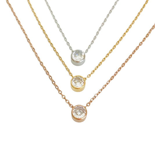 Three delicate necklace chains in rose gold, yellow gold, and silver, each featuring a bezel-set round clear gemstone pendant, arranged diagonally on a white background.