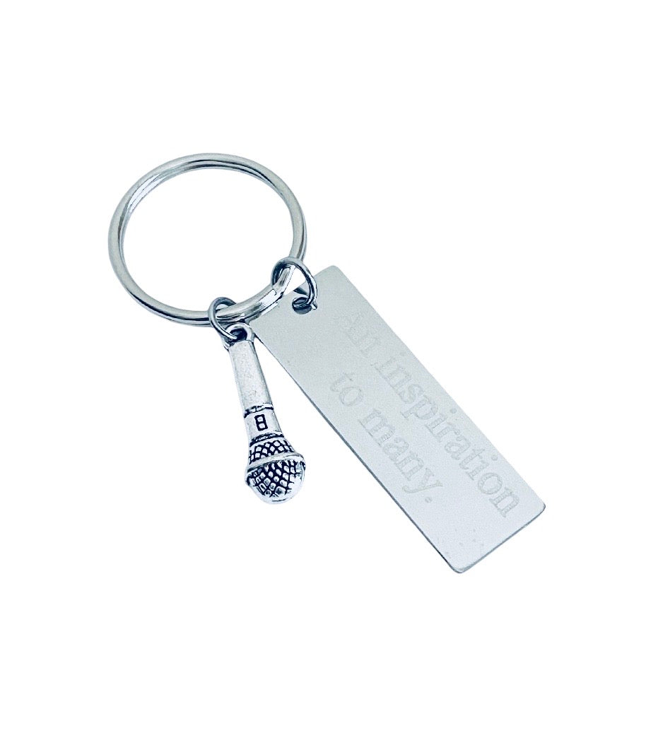 A silver metal keychain featuring a rectangular engraved tag that reads 'to many.' and a small microphone charm, shown on a plain white background.